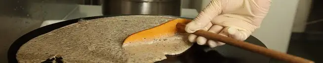 Crêpier étalant sa pâte à crêpe sur une billig